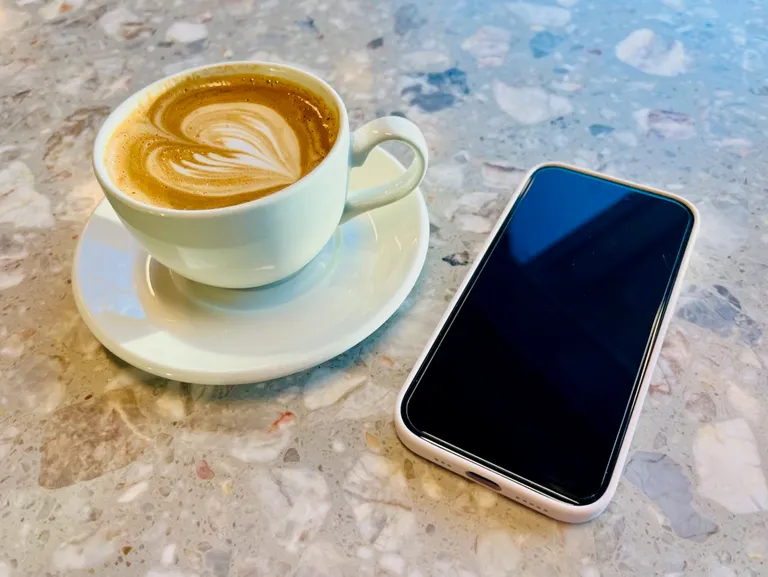 Bilde av en kontorplass hvor det ligger en mobiltelefon og en kaffekopp